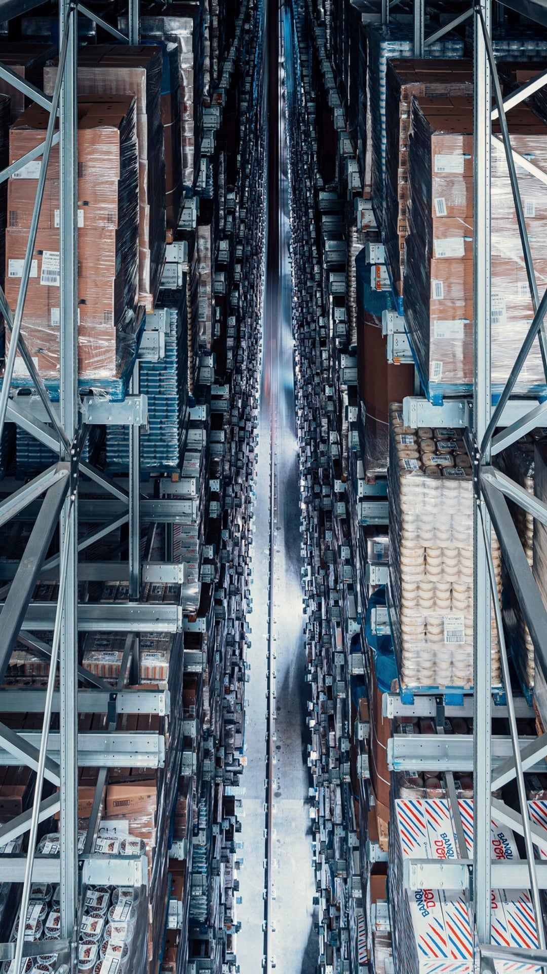 Bovenaanzicht van een smal magazijnpad tussen hoge stellingen vol pallets